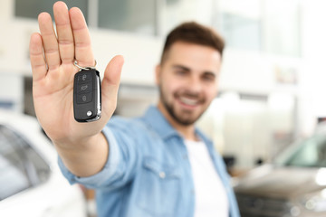 Happy man with key from new car in salon, closeup