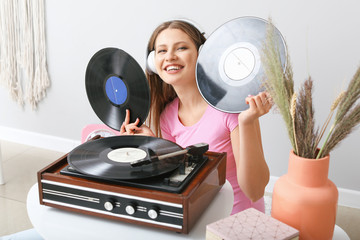 Beautiful young woman listening to music through record player at home