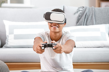 African-American teenager boy with virtual reality glasses playing video games at home