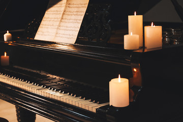 Stylish grand piano with burning candles in evening
