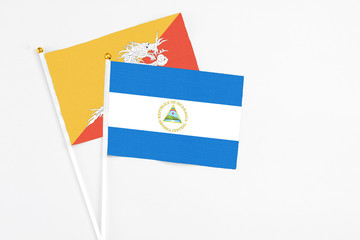 Nicaragua and Bhutan stick flags on white background. High quality fabric, miniature national flag. Peaceful global concept.White floor for copy space.