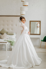 Pretty bride in a white dress stands in a room by the bed