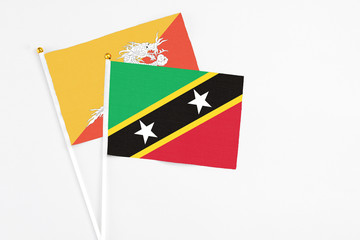 Saint Kitts And Nevis and Bhutan stick flags on white background. High quality fabric, miniature national flag. Peaceful global concept.White floor for copy space.