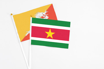 Suriname and Bhutan stick flags on white background. High quality fabric, miniature national flag. Peaceful global concept.White floor for copy space.