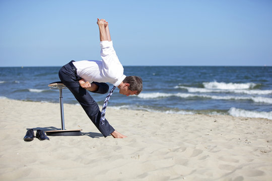 Caucasian business man exercising  on pneumatic stool  on the beach