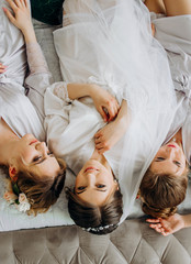 Sweet bride with bridesmaids in bathrobes lying on bed