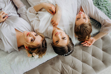 Pretty bride with bridesmaids in bathrobes lying on bed