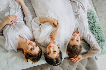 Amazing bride with bridesmaids in bathrobes lying on bed