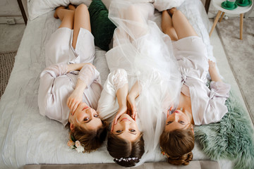 Cute bride with bridesmaids in bathrobes lying on bed