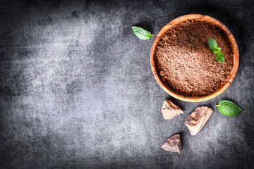 Cocoa beans and chocolate cacao powder with mint on top view. Copy space for text, dark stone table.