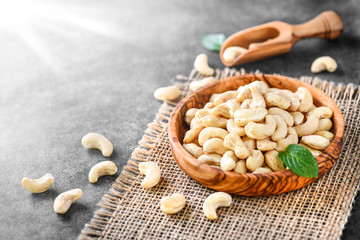Cashew nuts in olive wooden bowl on dark stone table. Delicacies nut on black background.