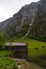 Fototapeta na wymiar Holzhütte an einem Bergsee mit Wald und Bergen an einem regnerischen woligen Sommertag