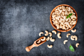 Cashew nuts in wooden bowl on dark stone table with mint leaf on top.