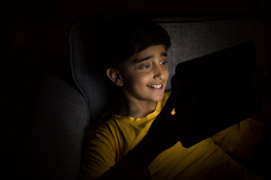 Portrait of a young boy using a tablet in the dark room. (Children)	