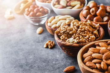 Mix nuts in wooden bowls on dark stone table. Almonds, pistachio, walnuts, cashew, hazelnut.