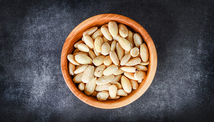 Peeled almond in wooden bowl top view on dark stone table. Almonds nuts concept.