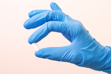 Hand in a blue medical glove with a white tablet on a light background. The concept of medicine, pharmacy, health. Minimalism, place for text.
