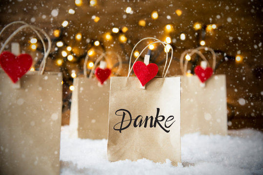 Christmas Shopping Bags On Snow With German Calligraphy Danke Means Thank You. Bright Glowing Lights In Background And Snowflakes