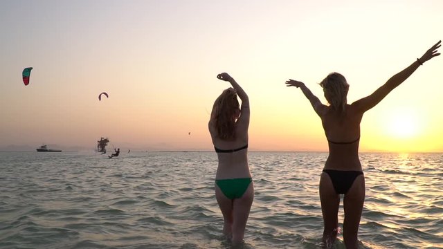 Two young women in bikinis are dancing in the sea, beach party