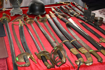 Many sabers, swords, spaces and daggers with helmet exhibited on red textile