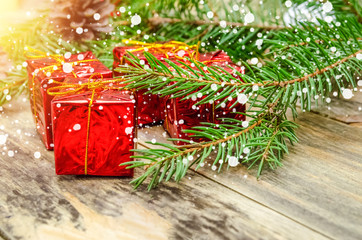 Red mini gifts on a wooden background among the branches of the Christmas tree and Christmas balls. Beautiful Christmas background