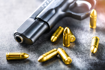 Hand gun with ammunition on dark stone background. 9 mm pistol gun military weapon and pile of bullets at the metal table.