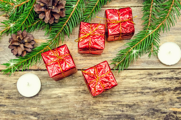 Red mini gifts on a wooden background among fir branches, candles, cones. Beautiful Christmas background with copy space. Photo of the top view.