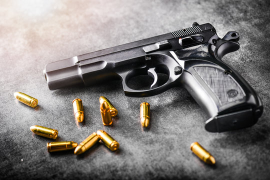 Hand gun with ammunition on dark stone background. 9 mm pistol gun military weapon and pile of bullets at the metal table.