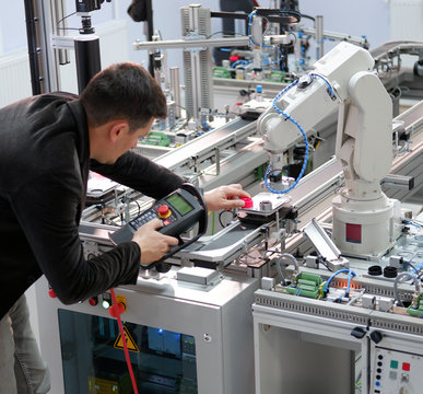 industry 4.0 concept: Man (engineer) is holding product and teaching robot arm the points with control panel (teach pendant) on smart factory production line background. Selective Focus.