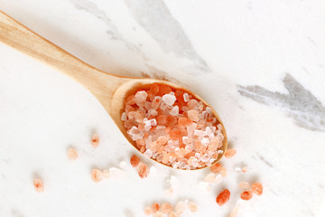 Fototapeta na wymiar top view of himalayan pink salt in wooden spoon on white marble table.