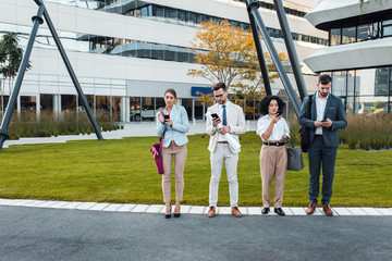 Business people standing outside of office buildings looking at their phones.  