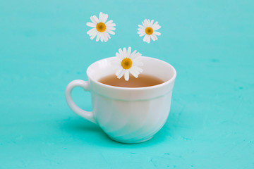 Chamomile tea, chamomile flowers fall in a white tea cup, turquoise background.