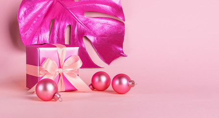 Festive box with a satin bow and golden neon toy balls on a pastel pink background . Holiday concept. Copy space