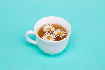 Chamomile tea in a white tea cup, chamomile flowers on the table. Place for text, copy-paste.