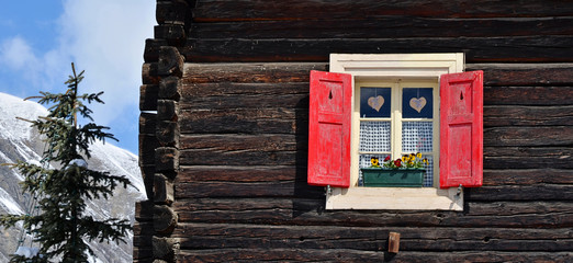 Window with open red shutters and heart in a typical wooden alpine chalet. Vintage cottage in mountains in Alps. Panoramic background with copy space.