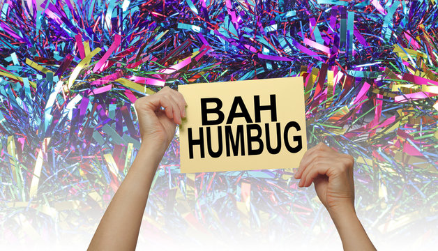 Bah Humbug for those who are fed up with over commercial Christmas - female hands holding placard with the words BAH HUMBUG against a graduated brightly coloured giant tinsel background