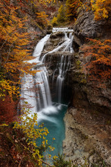 waterfall of water in the mountain through orange-leafed trees in a forest