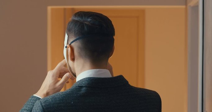 Anonymous man in suit hides his face with a mask and shows a gesture of silence. Masked Male holding a finger to his mouth, shows "TSS"