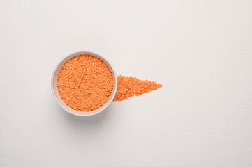 Bowl with lentils on a light textured background. Next to the grain is poured in the form of an arrow