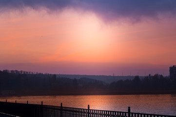 Unusual red sunset in a city park above the lake.