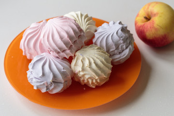 Multicolor marshmallows, fruity zephyr on an orange dish. Closeup of dessert with raspberry, blueberry and banana flavor.