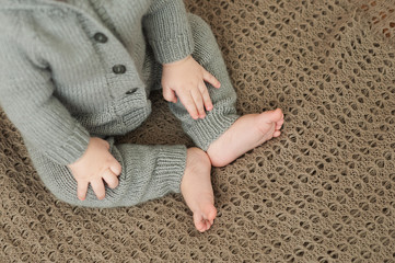 Fototapeta na wymiar baby hands and legs and heels of a child in a gray knitted suit sitting on a brown knitted warm plaid