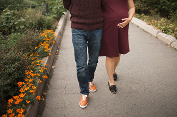  lovers with a pregnant girl in burgundy clothes, bright shoes with a man, walk in nature around the greenery and hold their hand on a pregnant belly with a baby