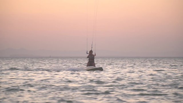Colorful sunset on the background of a young woman kitesurfing in the sea