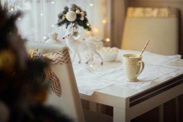  magical white and yellow glass of cocoa on a white table with gold napkins, with decorations of a white deer and white dishes in a bright cozy apartment for Christmas