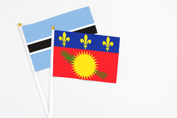 Naklejka premium Guadeloupe and Botswana stick flags on white background. High quality fabric, miniature national flag. Peaceful global concept.White floor for copy space.