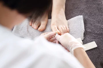 Photo sur Plexiglas Pédicure Nail clipping, foot care, female feet during a pedicure at a beauty salon. The beautician performs a pedicure treatment. Bare feet on a gray towel during care treatment. Natural photo no retouching.
