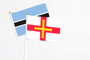 Guernsey and Botswana stick flags on white background. High quality fabric, miniature national flag. Peaceful global concept.White floor for copy space.