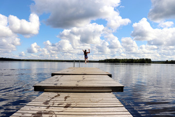 Girl jumping off the end of a pier at a lake in Finland