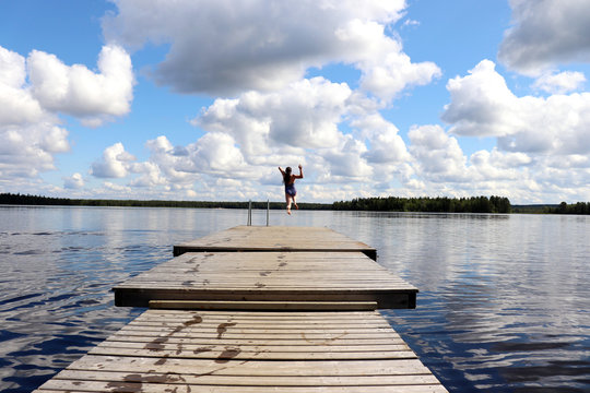 Girl Jumping Off The End Of A Pier At A Lake In Finland